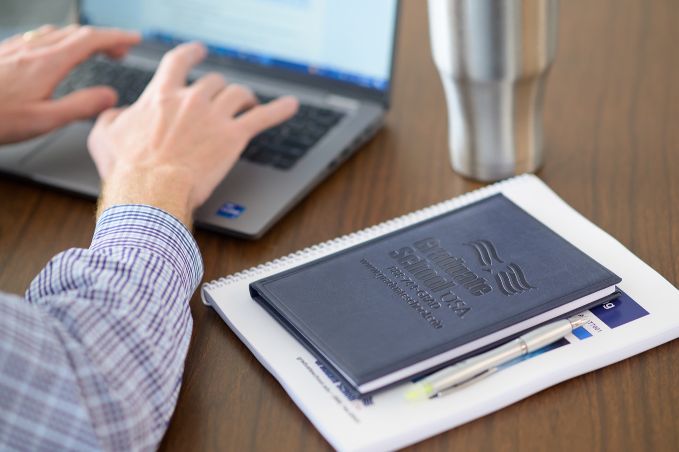 A learner working on a laptop beside Graduate School USA course materials